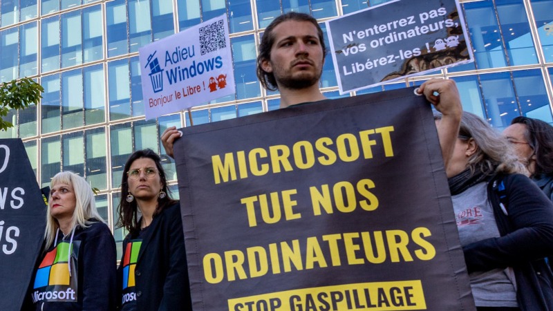 Une personne tient une banderole « Microsoft tue nos ordinateurs » devant le siège de Microsoft à Issy-Les-Moulineaux